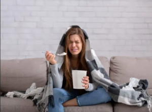 sentada en una sala, envuelta hasta la cabeza y con un bote enorme de helado, una adolescente llora desconsolada