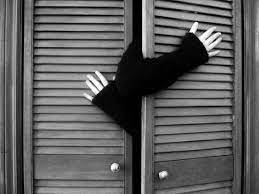 se ve la puerta de un clóset y unos brazos intentando salir de ahí. Los brazos tienen un suéter que llega hasta media mano y se ven desesperados por abrirlo