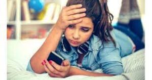 una chica de unos 20 años, acostada en la cama, mira a su celular con la misma cara de frustración que yo cuando intento entender las reglas sociales del WhatsApp